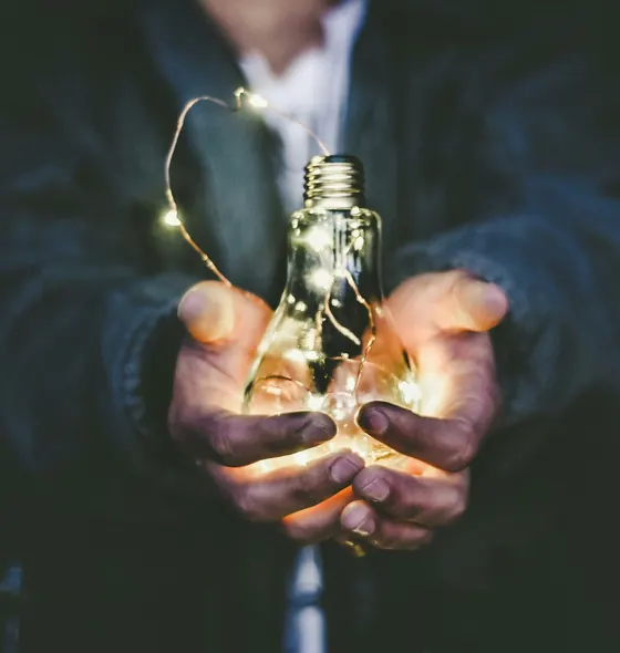 Hands cupping a glowing light bulb wrapped in fairy lights