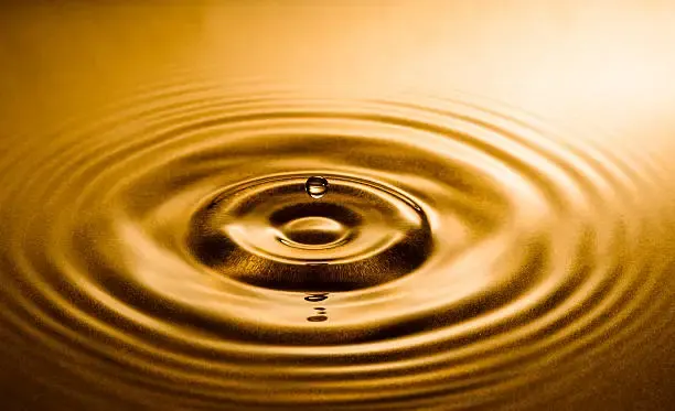 A single gold drop sending ripples across still water